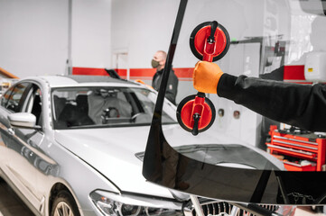 Automobile technician worker replacing windscreen or windshield of a car in auto service station...