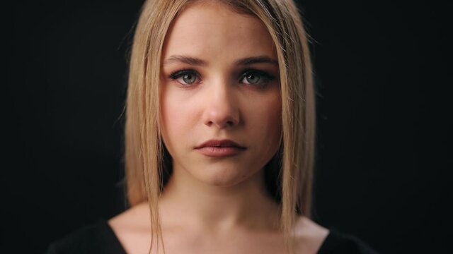 Close up of serious blonde with light make up in casual sweater. Young woman isolated over black studio background. Female appearance.
