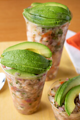 A view of several different size cups filled with ceviche and avocado slices.