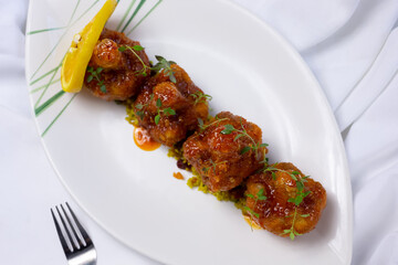 A top down view of a plate of buffalo wings style cauliflower florets, in a restaurant or kitchen setting.