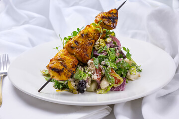 A view of a plate of chicken kabob salad, in a restaurant or kitchen setting.
