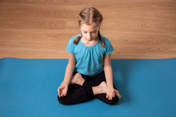  Little girl sitting on the roll mat practicing meditate yoga at home