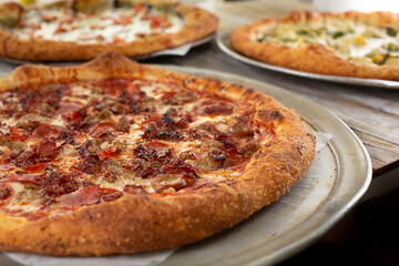 A view of a meat lovers pizza on a table surface with several other pizzas.