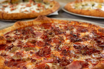 A view of a meat lovers pizza on a table surface with several other pizzas.