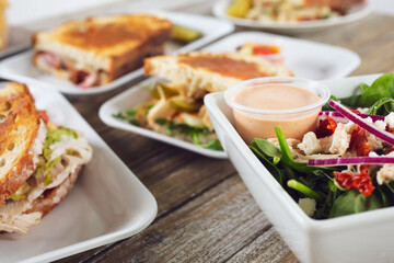 A view of several sandwich entrees on a table, featuring a bowl of salad, in a restaurant or kitchen setting.