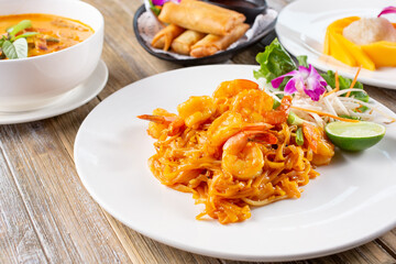 A view of several Thai entrees on a table, featuring pad Thai, curry soup, and mango sticky rice.