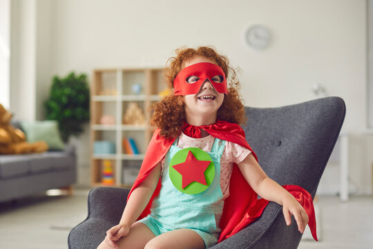 Portrait of laughing happy red haired girl in costume of superhero star sitting on armchair and smiling
