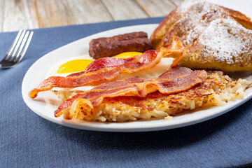 A view of a French toast breakfast plate, featuring sunny side up eggs and bacon strips.