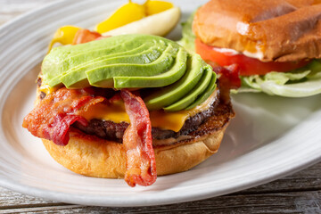 A closeup view of an open faced bacon avocado cheeseburger on a plate.