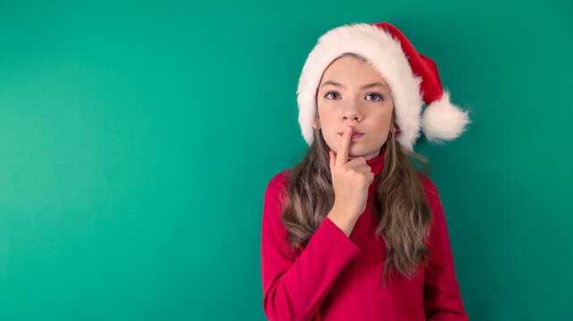 Happy Christmas girl in a red suit and a Santa Claus hat on a green background. Red and green. Portrait of child. Thoughtful look. Space for copying.