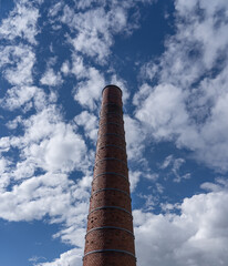 Tall chimney on a bright sunny day with clouds seen from the earth - 395978567