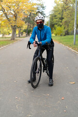 An athlete in glasses and a protective mask stands on a bicycle in a park on a bicycle road. Quarantined sports and outdoor recreation.