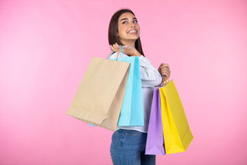 Amazing brunette girl posing with shopping bags. Shopping woman happy smiling holding shopping bags isolated on pink background. Shopping, sales, black friday concept.