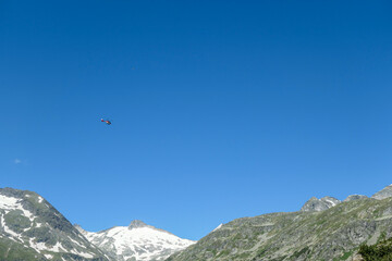A rescue helicopter flying over the Alps in Austria. Rescue mission in a difficult terrain. There are high, snow capped mountains around. The helicopter flies high above the peaks