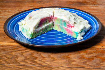 cooking sweet sponge cake at home - sliced homemade colorful sponge cake with whipped cream on blue plate on wooden table at home kitchen