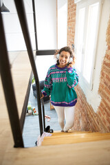 Young, smiling girl walking up the stairs inside her house. She is wearing a headphone. Space for...