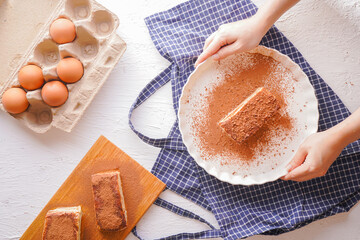 Delicious Tiramisu - traditional italian dessert from mascarpone cheese and biscuit. gourmet tiramisu dessert topped with chocolate powder served on a white plate at table background.