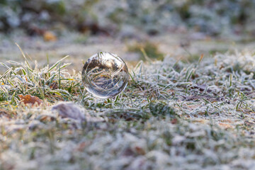 A photographic crystal ball lies on frozen grass. The grass reflects grass covered with ice crystals.