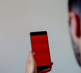 View of man's hands holding a smartphone with a red space screen for your text message or information content