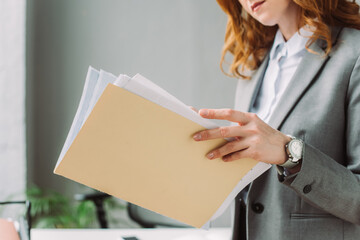 Cropped view of businesswoman leafing through paper sheets in folder with blurred workplace 