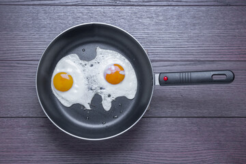 fried eggs from two eggs in a frying pan on a wooden background, top view, flat lay food