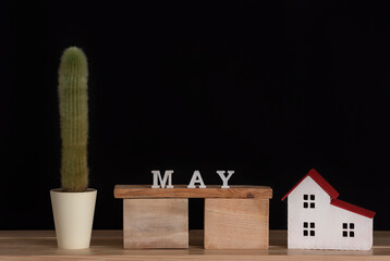 Wooden calendar of May, cactus and house model on black background. Copy space