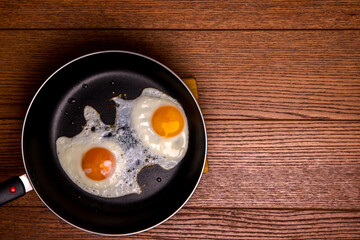 fried eggs from two eggs in a frying pan on a wooden background, top view, flat lay food, copy space