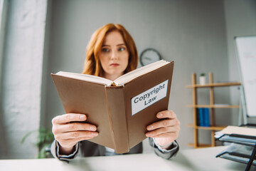 Low angle view of book with copyright law lettering in hands of female lawyer sitting at workplace...
