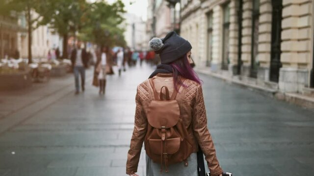 Pretty girl rear view enjoying spring outdoors. City lifestyle. Stylish hipster woman tourist walking on old town street. Lady in leather jacket portrait walk through the city during travel vacation.