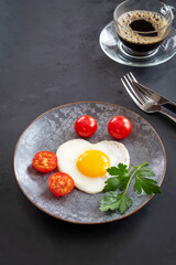 Breakfast with fried eggs, tomatoes and a cup of coffee. Fork and knife on a black background. Copy space. Table setting for valentine's day.	