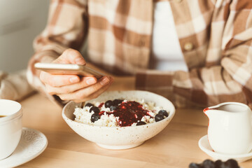 Woman is looking for information on Internet, using mobile, during eating breakfast. Concept for digital addiction.