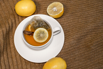 Lemon tea with cinnamon in a white Cup on a saucer stands on a warm sweater with lemons
