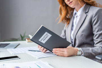 Cropped view of female lawyer holding book with intellectual property lettering at workplace on...