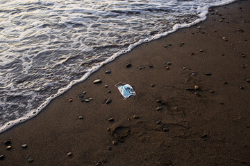 medical mask thrown on a sandy sea beach and polluting it
