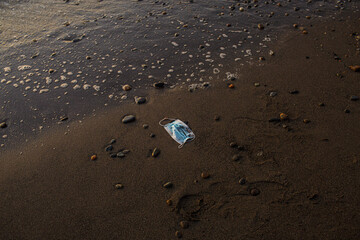 face mask thrown on a sandy sea beach and polluting it
