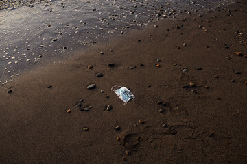 face mask thrown on a sandy sea beach and polluting it