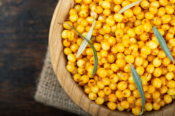 Sea buckthorn. Fresh ripe berry in wooden bowl with leaves on wood background. Flat lay pattern