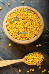 Sea buckthorn. Fresh ripe berry in wooden bowl and a spoon with leaves on wood background.