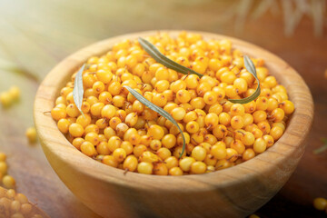 Sea buckthorn. Fresh ripe berry in wooden bowl with leaves on wood background.