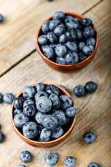 Fresh blueberries in a clay bowl and scattered on a wooden table. Foods containing antioxidants.