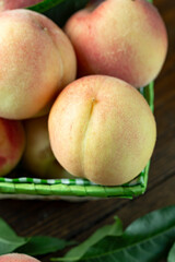 Fresh harvest of peaches in a basket on a wooden rustic table. Peach leaves are present in the composition.