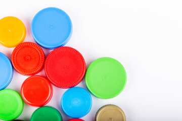 Many multi-colored plastic bottle caps on a white background.