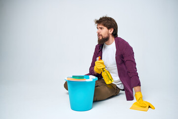 A man lies on the floor with a bucket of detergent cleaning service light background