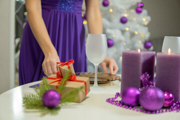 Obraz na płótnie Canvas girl makes Christmas table decoration with gifts and purple candles.
