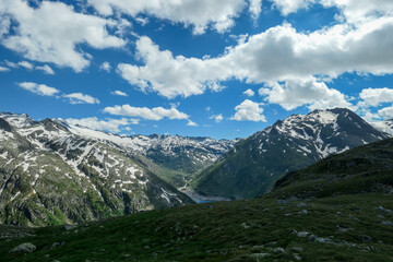 Fototapeta premium Panoramic view on huge glacier in Maltal region in Austrian Alps. The valley below it flourishing with green and freshness., small torrent in the middle. Summer in the mountains. Serenity and solitude