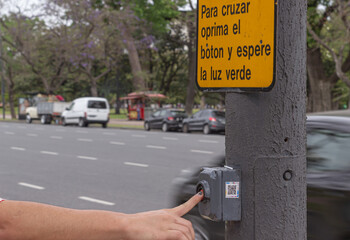 Sign indicating: to cross, press the button and wait for the green light. Hand pressing the button.