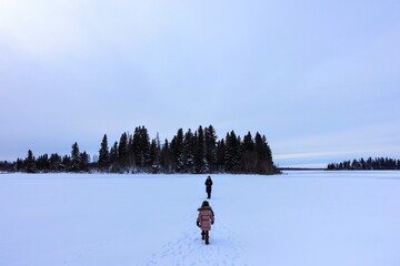 A mother and her daughter walking along the frozen Astotin Lake on a snowy winter day admiring the...