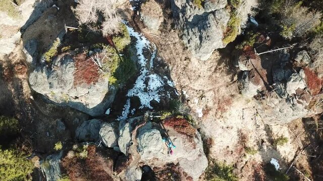 A top down capture of a couple standing at the top of rock formation hiding between tall forest in Austrian Alps. Early spring in Alps. The nature wakes up after hibernation. Adventure and achievement
