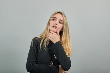 Hand on chin thinking about question, pensive expression. Doubt. Thoughtful face. Using that incredibly sharp business mind. Young attractive woman, dressed black sweater with green eyes, blonde hair
