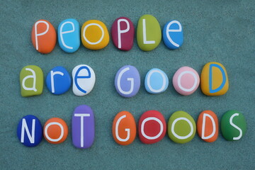 People are good not goods, social slogan composed with multicolored stone letters over green sand